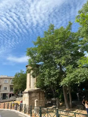 a tree and a monument next to a fence at Cozy tiny apartment in the heart of Plaka in Athens