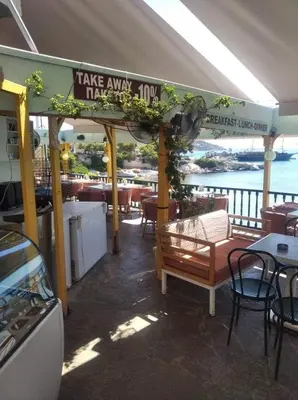 a restaurant with tables and chairs and a view of the water at Ammoudia Rooms in Agia Marina Aegina