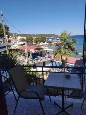 a table and chair on a balcony with a view of the ocean at Ammoudia Rooms in Agia Marina Aegina