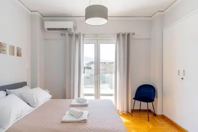 a white bedroom with a bed and a blue chair at Koukaki Spacious Penthouse with parking for Small Car in Athens