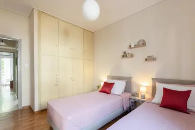 two beds in a bedroom with white walls and red pillows at Heart of Koukaki flat, near Acropolis & Filopappou in Athens