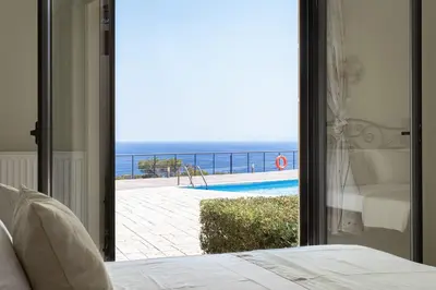 a bedroom with a view of a swimming pool and the ocean at Aphaia Villa & Residences Aegina in Agia Marina Aegina