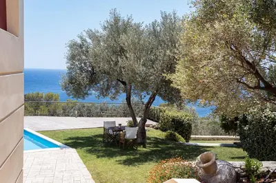 a garden with a table and a tree next to a swimming pool at Aphaia Villa & Residences Aegina in Agia Marina Aegina