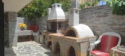 a patio with a stone fireplace with a red chair at SHLEY House 1 in Artemida