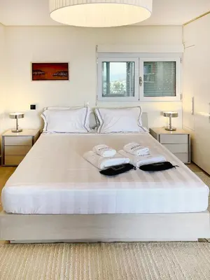 a bedroom with a large white bed with two towels at Blue Bay Vouliagmeni Luxury Apartment in Athens