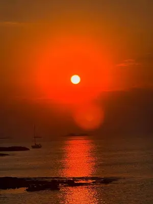 a sunset over the ocean with a boat in the water at The Dona House in Vaia