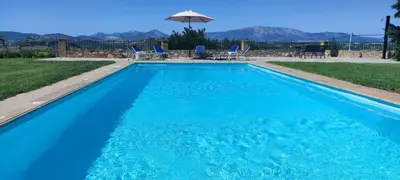 a blue swimming pool with chairs and an umbrella at Ellie's StoneHouse Gianapa, Porto Rafti, Greece, 190 03, GR in Porto Rafti