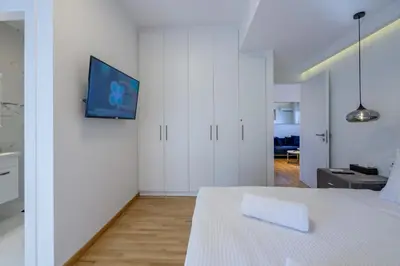 a white room with a bed and a tv on a wall at Lush Sapphire apt steps from Acropolis & Plaka! in Athens