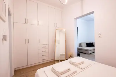 a white bedroom with a bed and a mirror at Eden - A Night near Athens Int Arpt in Spáta