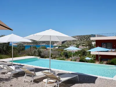 a swimming pool with chairs and umbrellas at Augoustos ECO luxury apartments with pool in Aghia Marina