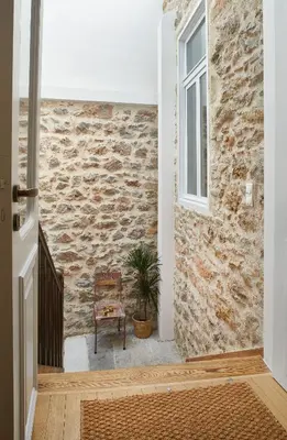 a hallway with a stone wall and a chair and a window at Chloe Boutique Apartments Plaka in Athens