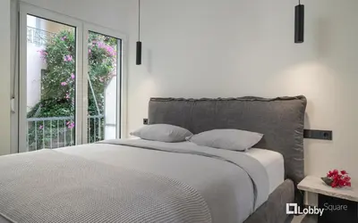 a white bedroom with a bed and a window at La Mer Apartment by LobbySquare in Piraeus