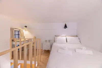 a bedroom with a bed with white sheets and a staircase at Stoa Kairi Loft A in Athens