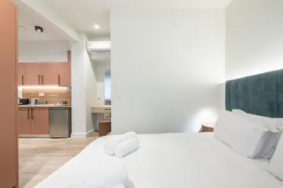 a bedroom with a white bed and a kitchen at Aeiphoria Suites & Rooms - Athens in Athens