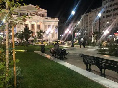 a person sitting on a bench in a park at night at Royal Red suite No2 PIRAEUS PORT in Piraeus
