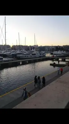 a group of people walking on a sidewalk near a marina at Piraeus historical center in Piraeus