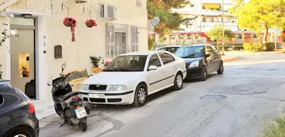 a white car parked next to a motorcycle on a street at Bella Ciao Guest House in Athens