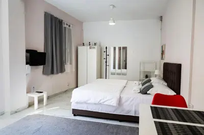 a white bedroom with a bed and a red chair at Lysandros Apartments in Athens, near the METRO in Athens