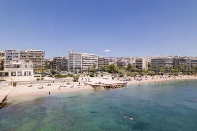 a beach with people in the water and buildings at Lovely seaside apartment next to Starbucks opposite the beach park of Flisvos in Athens