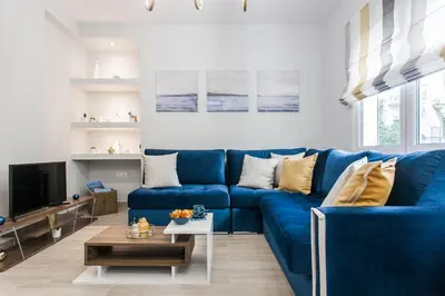 a living room with a blue couch and a tv at Lovely seaside apartment next to Starbucks opposite the beach park of Flisvos in Athens