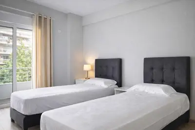 two beds in a white room with a window at Acropolis Area Large 3BR 2BA Apartment in Athens