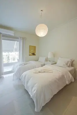 a white bedroom with two beds and a window at LucyZen! Stylish Apt, Athenian Riviera, near beach in Athens