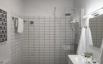 a white tiled bathroom with a shower and a sink at Aether Apartment by LobbySquare in Athens