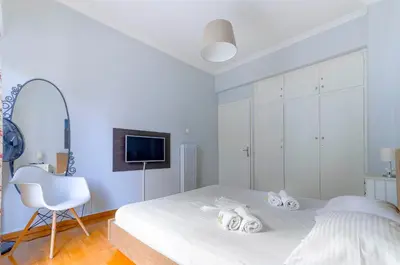 a white bedroom with a white bed and a chair at Spacious 2BA next to the park and Archeological museum in Athens