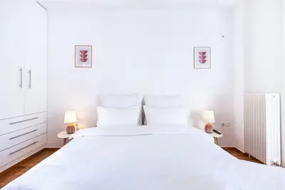 a white bedroom with a large white bed with two lamps at Loft Apt with Acropolis View in Athens