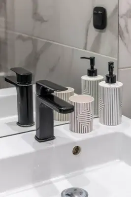a bathroom sink with a black faucet and three toilets at The HostMaster Artistic Inn in Athens