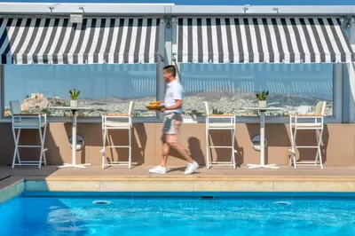 a man walking past a pool on the rooftop of a hotel at Divani Caravel in Athens