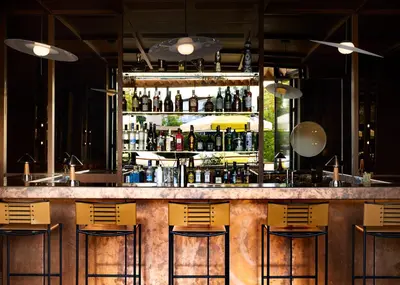 a bar with yellow chairs and bottles of alcohol at Ace Hotel & Swim Club Athens in Athens
