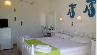 a white bedroom with two beds and a mirror at Rachel Hotel in Agia Marina Aegina