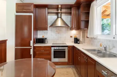 a kitchen with wooden cabinets and a stainless steel appliance at Phoceus Poolfront Grande Villa in Palaiá Fókaia