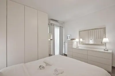 a white bedroom with a white bed and a mirror at Belva Blue Glyfada Modern 2BR Walk to Ctr & Beach in Athens
