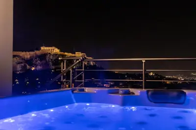 a hot tub with a view of the acropolis at night at Majestic Acropolis-Lycabettus in Athens