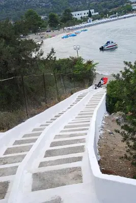 a concrete walkway next to a beach with a boat at The Delfini Hotel in Agia Marina Aegina