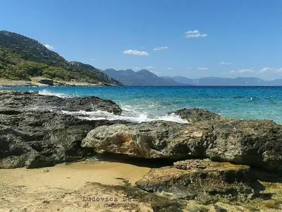 a beach with rocks and the ocean and mountains at The Delfini Hotel in Agia Marina Aegina