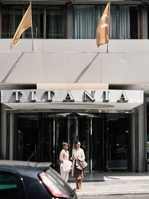 two people walking in front of a building with a sign at Titania Hotel in Athens