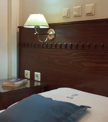 a bed with a wooden headboard and a table with a lamp at Triton Hotel Piraeus in Piraeus