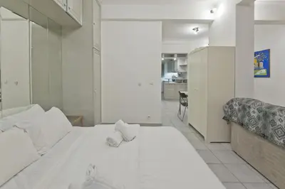 a bedroom with a large white bed and a kitchen at Mavili Square Cozy Apt AC & Kitchen, near Metro in Athens