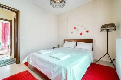 a bedroom with a large white bed with a red rug at Escape with Style in this Chic 2BR Apartment! in Athens