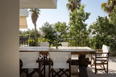 a wooden table and chairs on a patio with palm trees at Voula Riviera Apartment in Athens