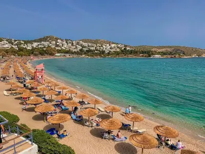 a beach with umbrellas and people sitting on the beach at South Blue Luxury Apartment in Vouliagmeni in Athens