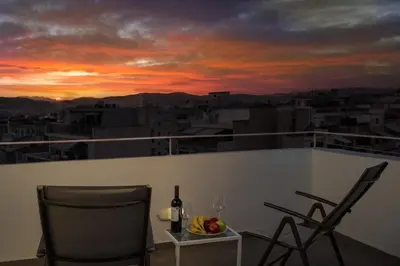 a table and chairs on a balcony with a sunset at Olvar Penthouse Apartment in Athens