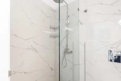 a shower with white marble walls and a glass door at A newly fully renovated studio in Athens
