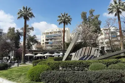 a sculpture in a park with palm trees and a building at Comfortable apt, next to Archeological museum! in Athens