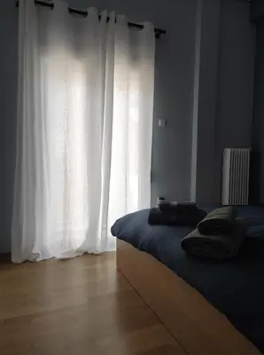 a bedroom with a bed and a window with white curtains at Comfy in Kypseli in Athens