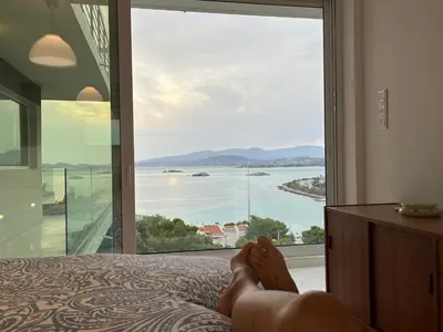 a person laying on a bed in front of a large window at Luxurious 2-Bed Seaside Apartment in Saronida in Saronida