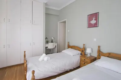 two beds in a bedroom with white walls and wood floors at Andromaxi 2BR Apt near SNFCC, AC, WiFi in Athens